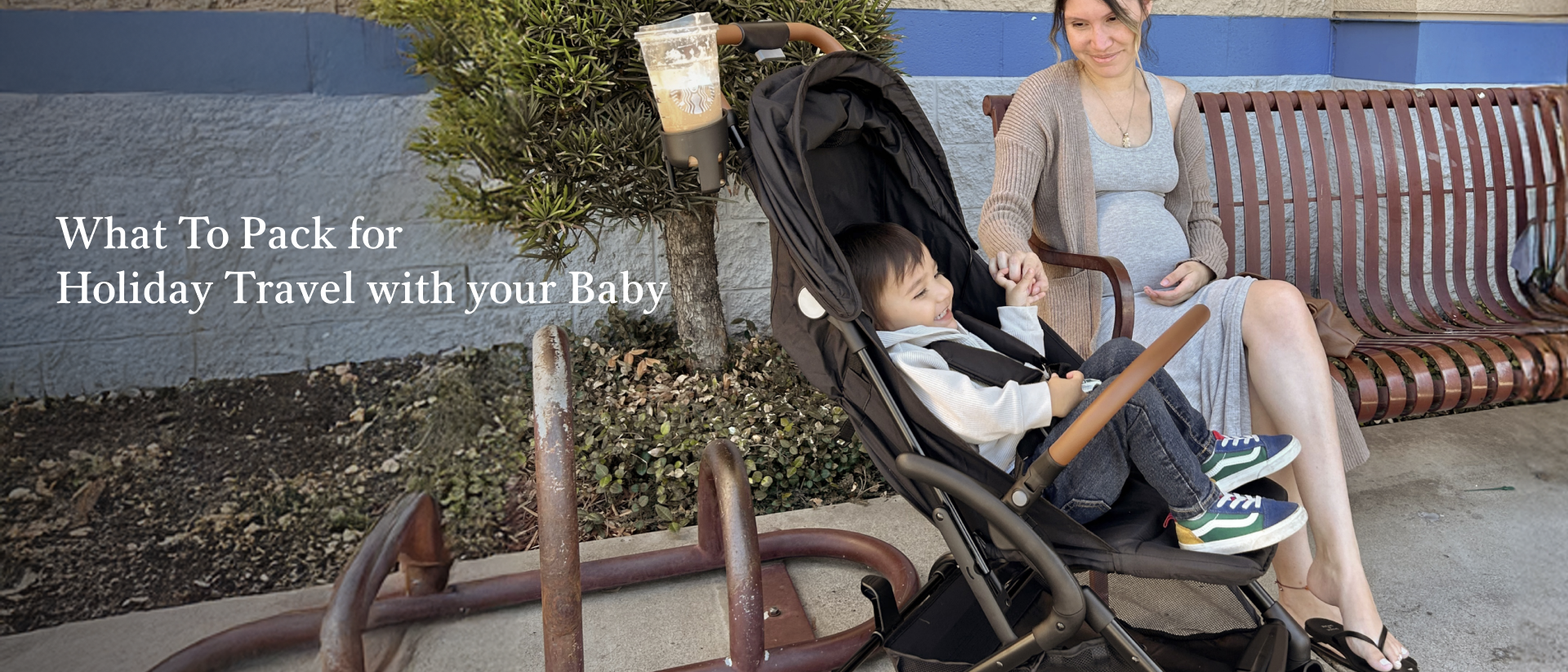 Mother sitting on a bench smiling at her young child in a Dream On Me RioGlide stroller during holiday travel.