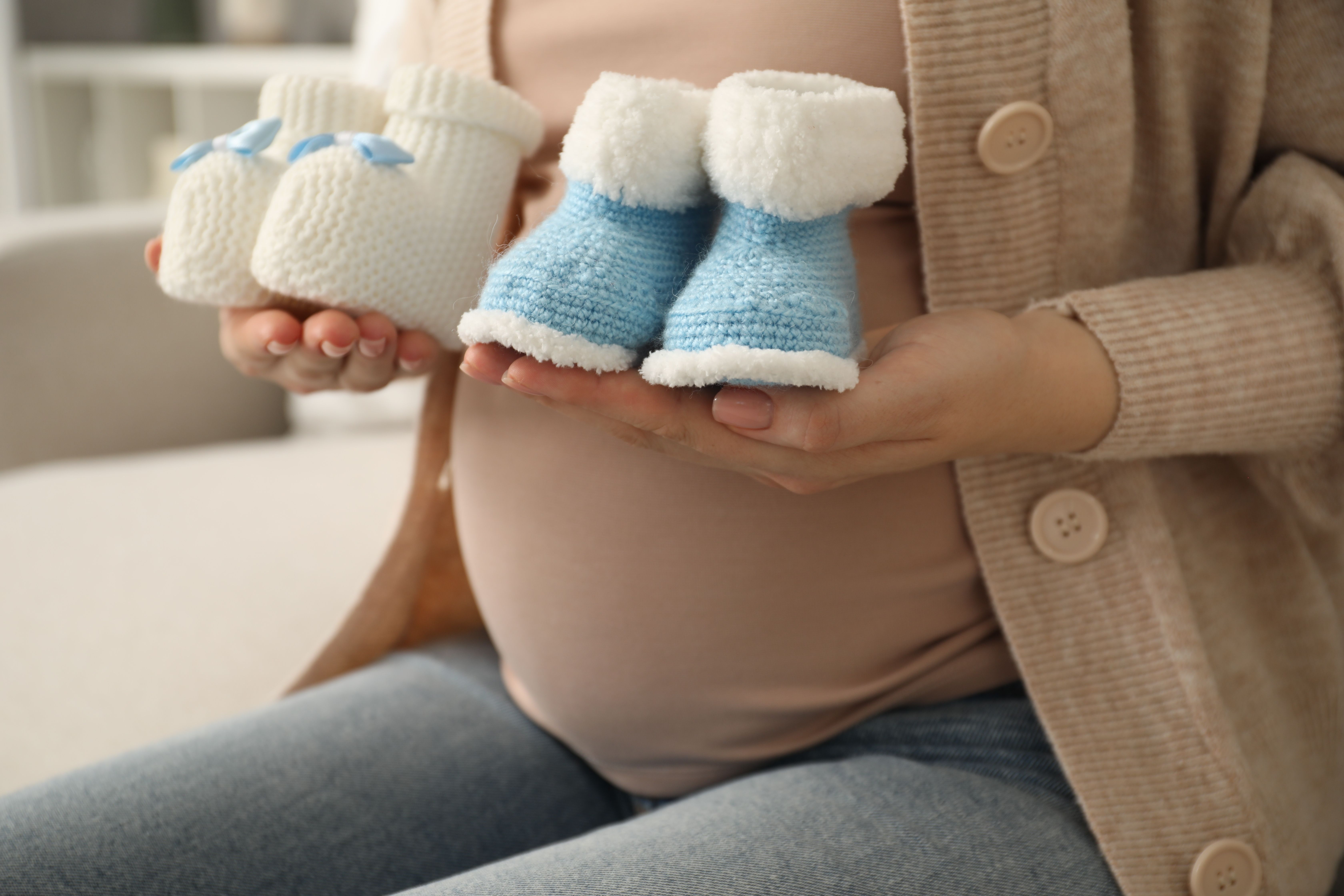 Pregnant woman holding two pairs of knitted baby booties showing twin pregnancy