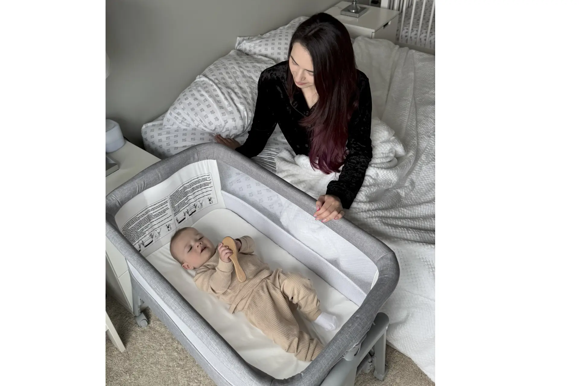 Infant playing in Dream On Me Calypso Portable bassinet next to mother in modern bedroom