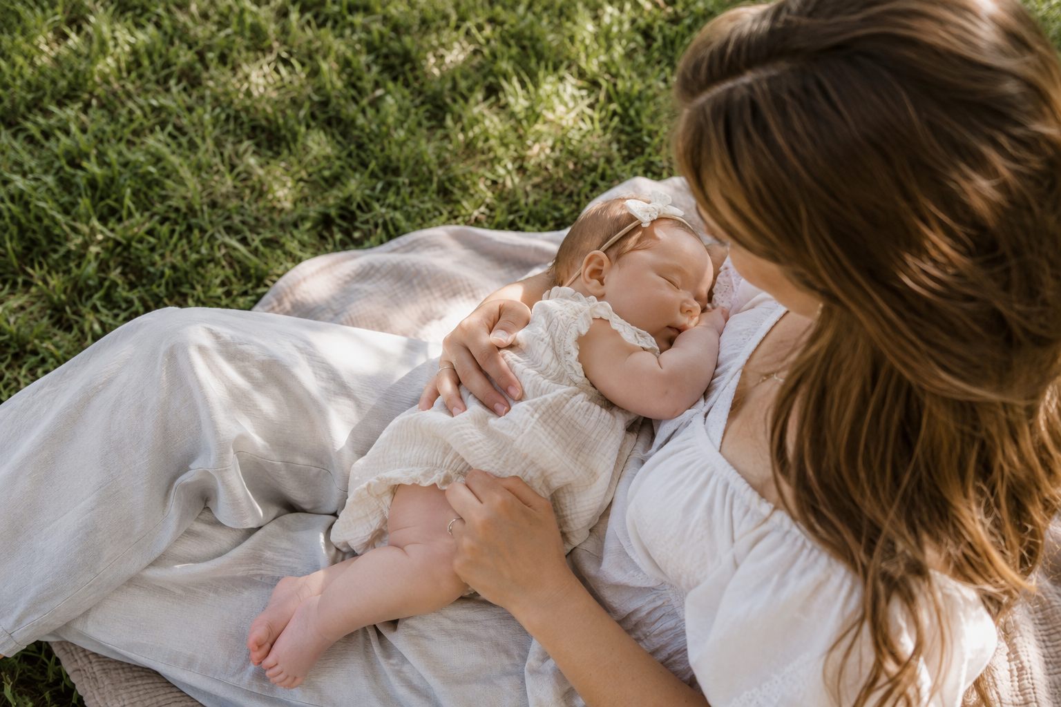 A woman cradles a sleeping baby on a blanket on green grass.