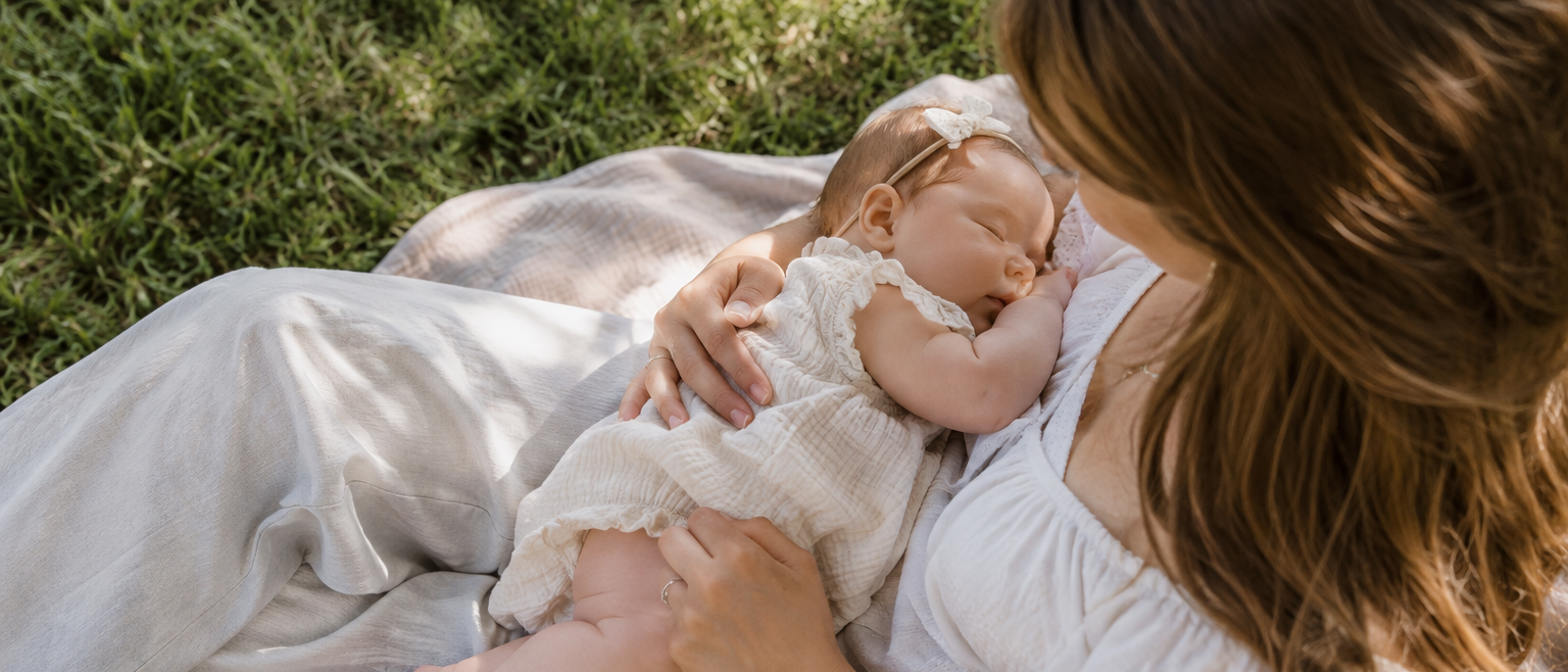 A woman cradles a sleeping baby on a blanket on green grass.