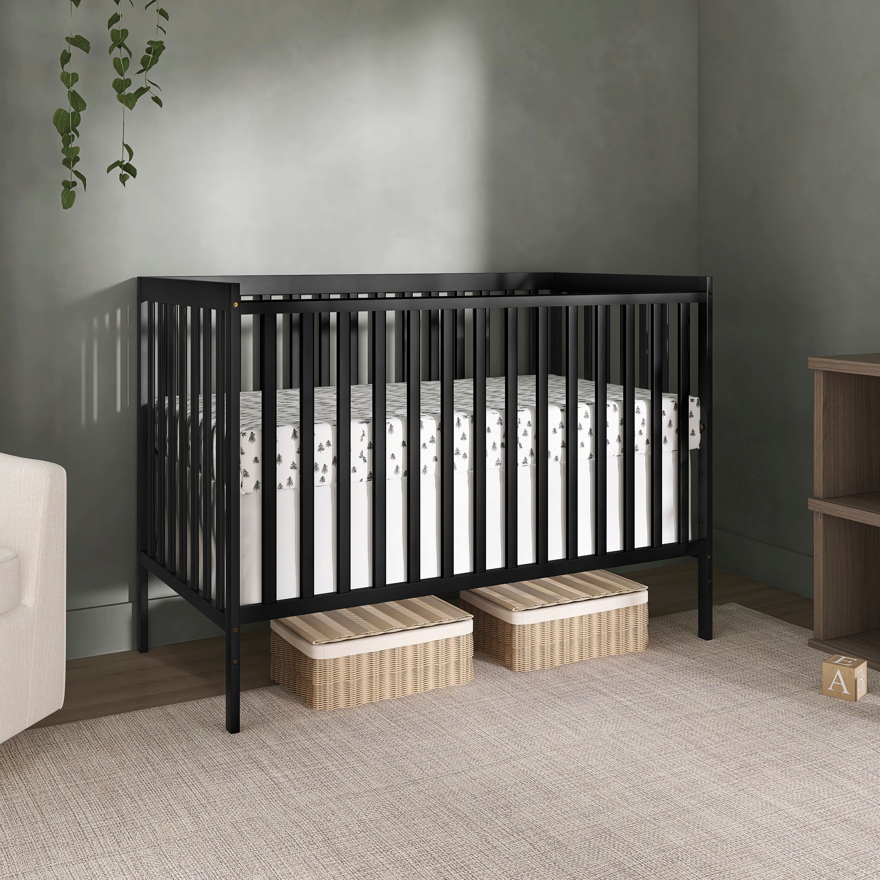 Dream On Me Synergy 5-in-1 convertible crib in black with a mattress, placed in a modern nursery with storage baskets underneath