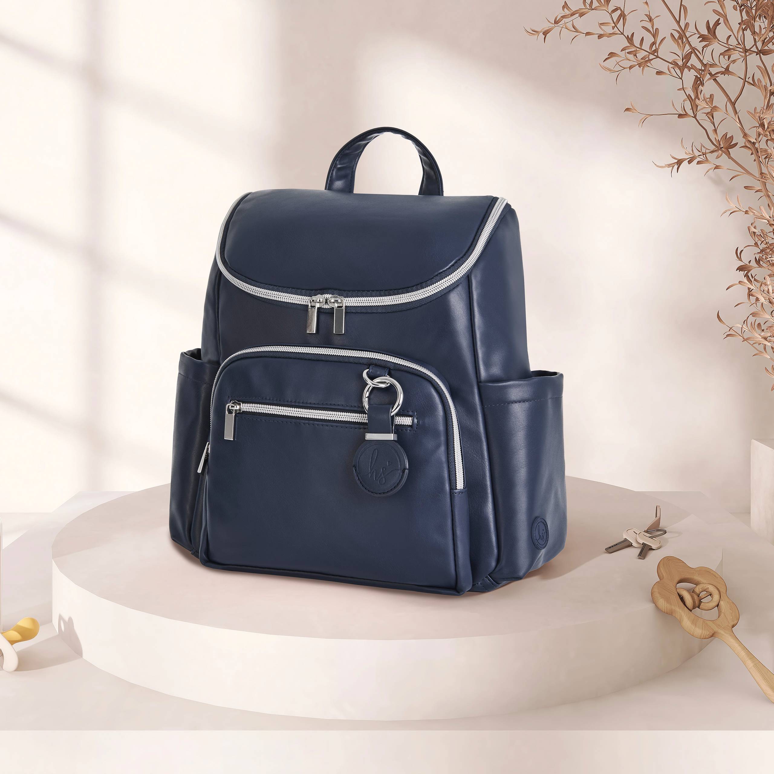 Navy blue diaper bag displayed on a neutral pedestal against a soft beige background with warm lighting and minimal nursery-inspired accents