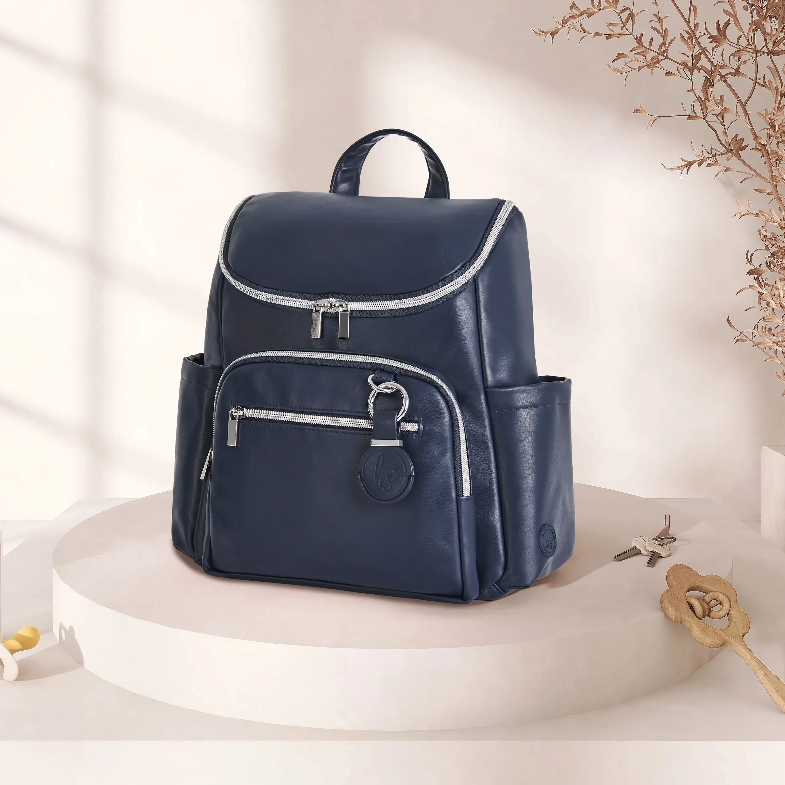 Navy blue diaper bag displayed on a neutral pedestal against a soft beige background with warm lighting and minimal nursery-inspired accents
