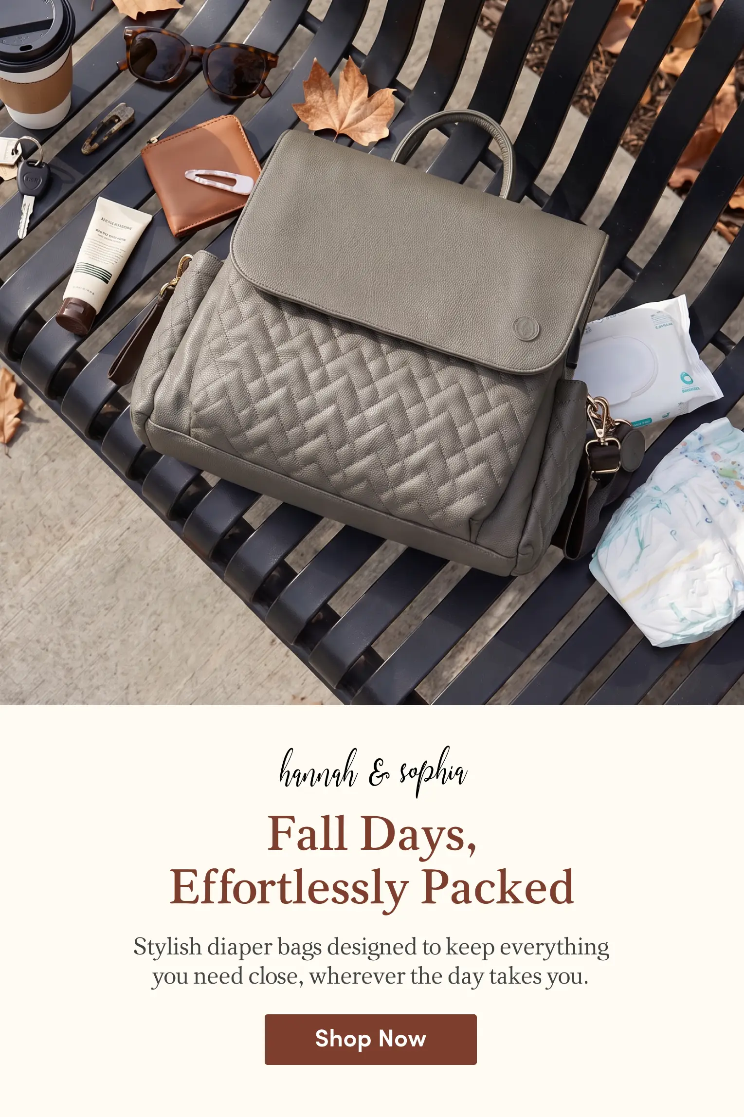 A grey quilted diaper bag and daily essentials like baby wipes, a diaper, coffee, and sunglasses are arranged on a black bench with fall leaves. Promotional text for Hannah & Sophia reads "Fall Days, Effortlessly Packed."