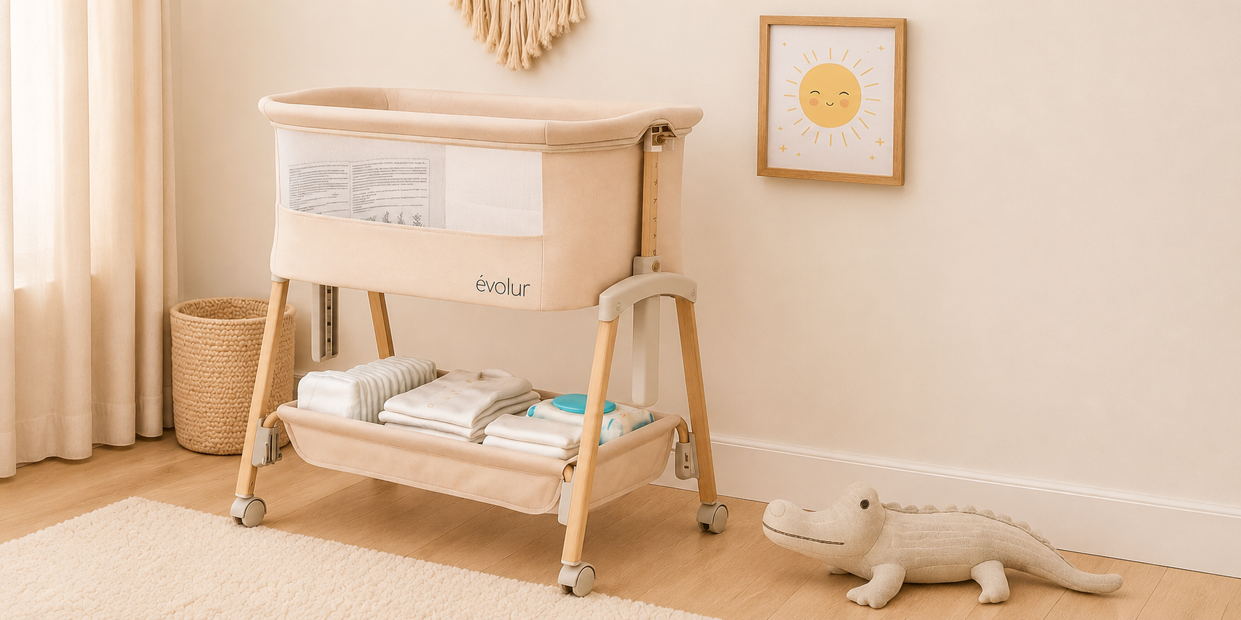 A beige Évolur baby bassinet with storage below, in a softly lit nursery with an alligator toy and sun picture.