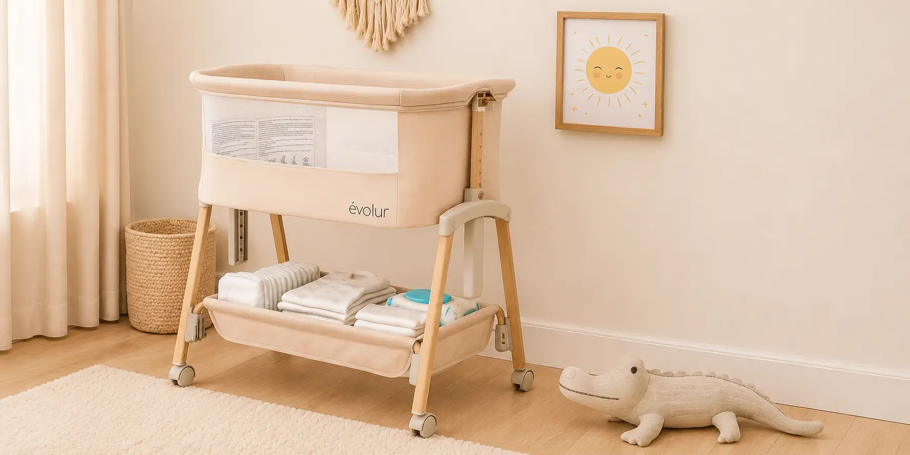 A beige Évolur baby bassinet with storage below, in a softly lit nursery with an alligator toy and sun picture.