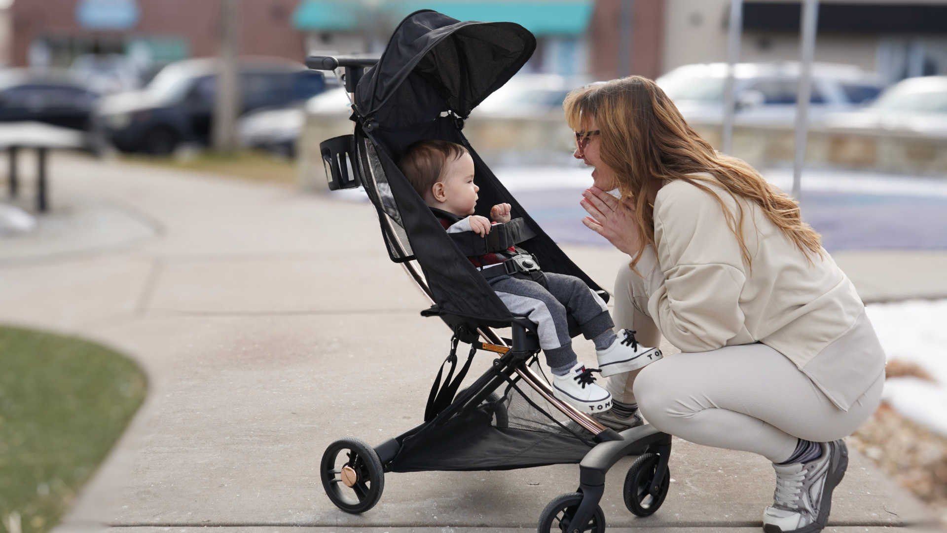 Mother interacting with baby seated in a Evolur Roamer Ultra Light Stroller in black during a walk on a city sidewalk