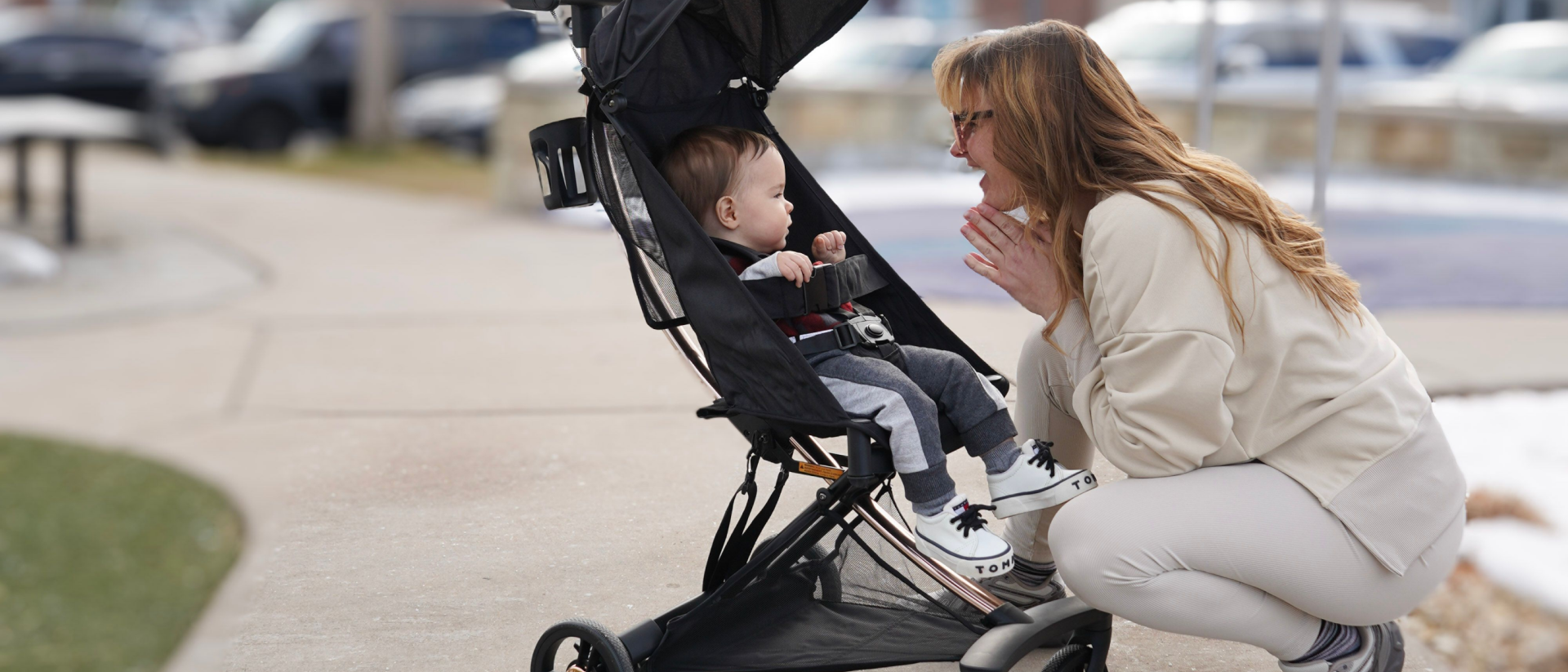 Mother interacting with baby seated in a Evolur Roamer Ultra Light Stroller in black during a walk on a city sidewalk