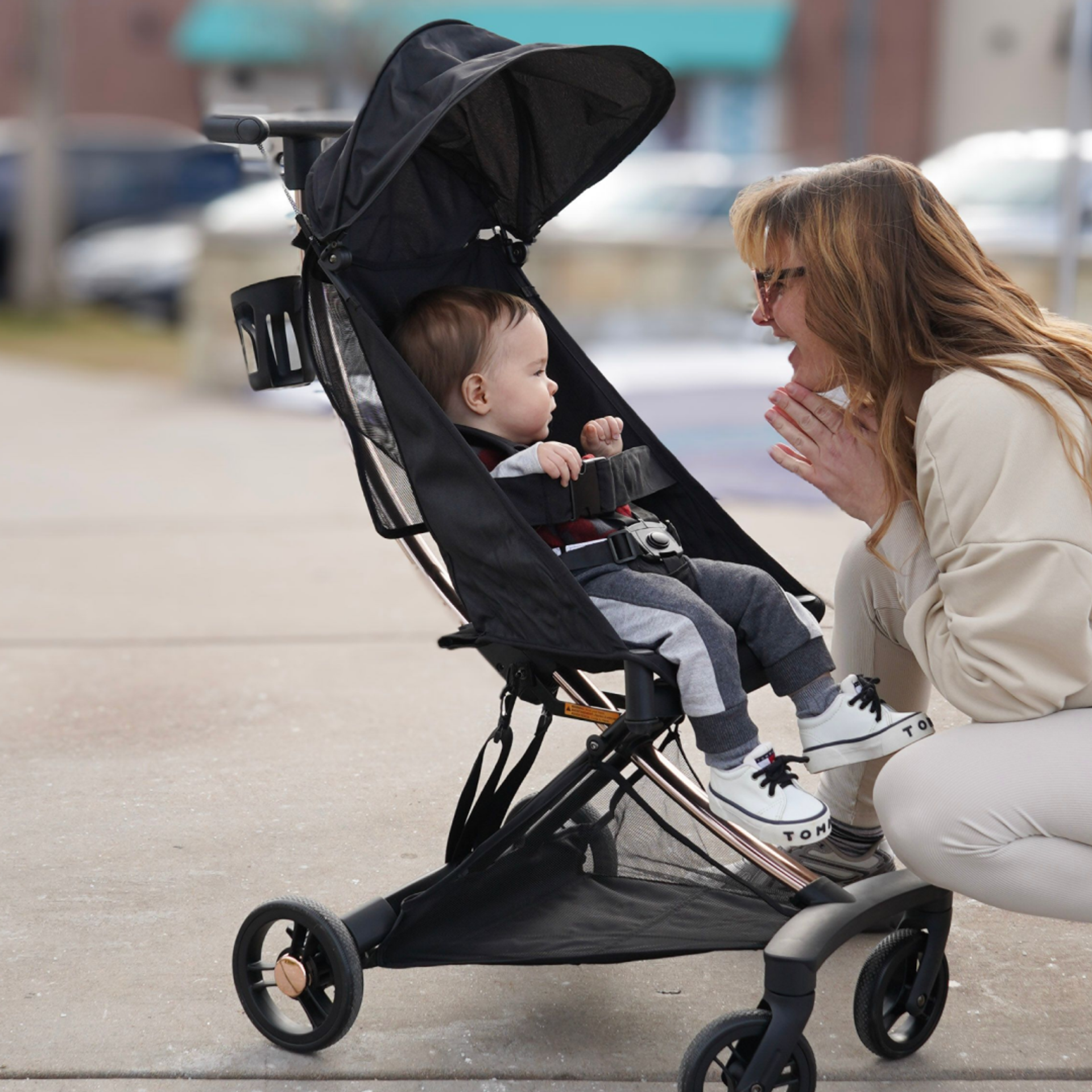 Mother interacting with baby seated in a Evolur Roamer Ultra Light Stroller in black during a walk on a city sidewalk