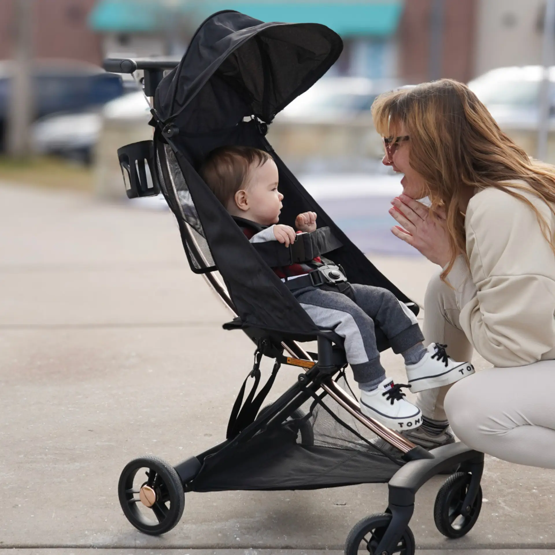 Mother interacting with baby seated in a Evolur Roamer Ultra Light Stroller in black during a walk on a city sidewalk