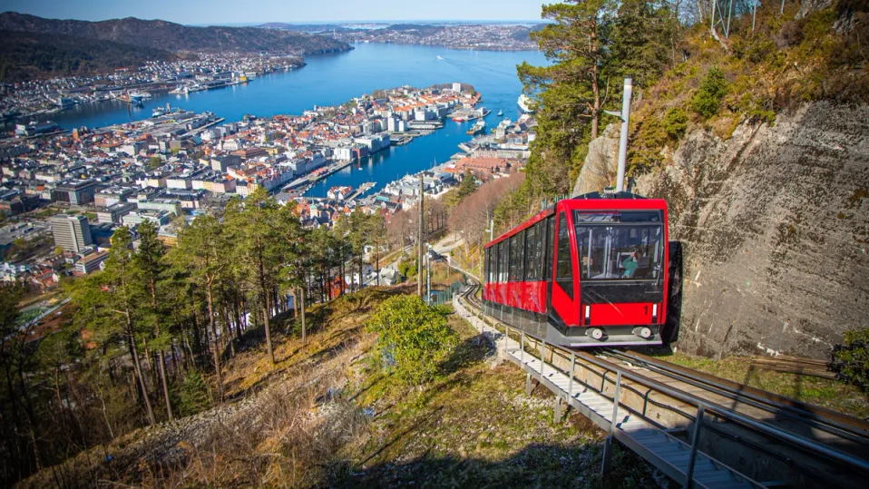 a red cable car is going up a hill with a city in the background .