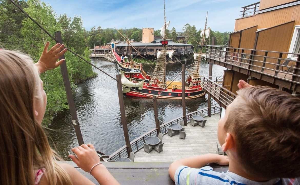 a boy and a girl are looking at a pirate ship in the water .