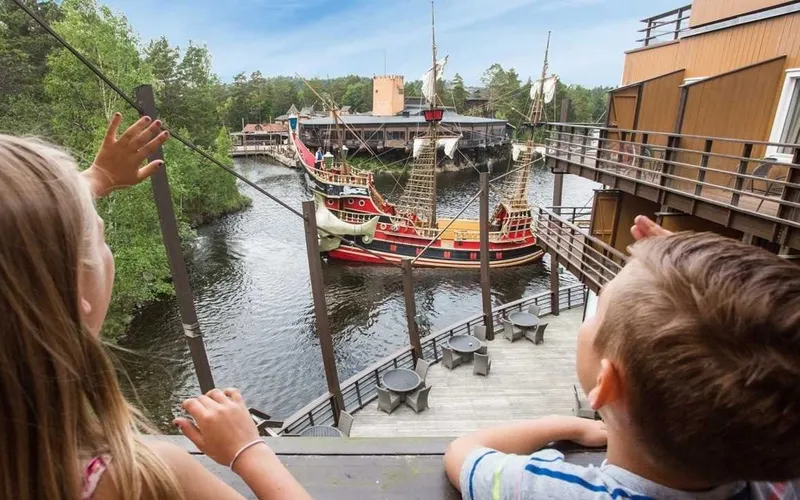 a boy and a girl are looking at a pirate ship in the water .