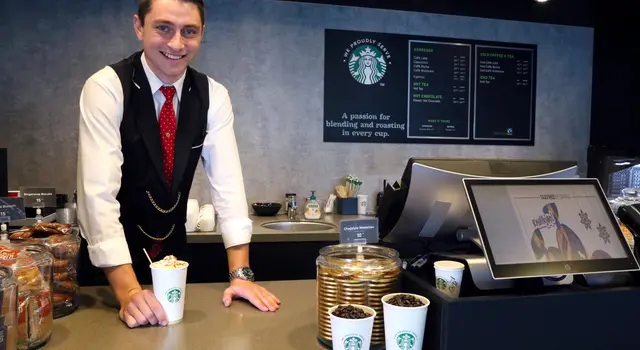 ein Mann im Anzug und Krawatte steht hinter einer Starbucks-Theke.