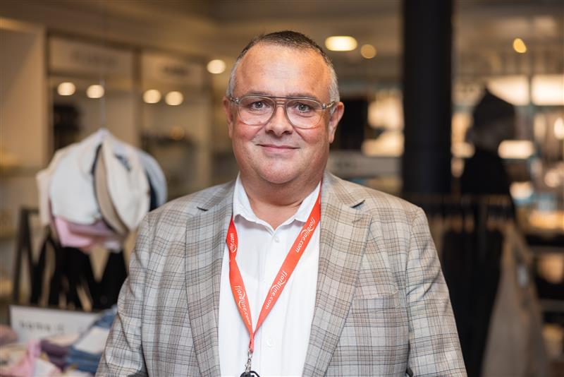 A man wearing glasses and a lanyard is standing in a store.