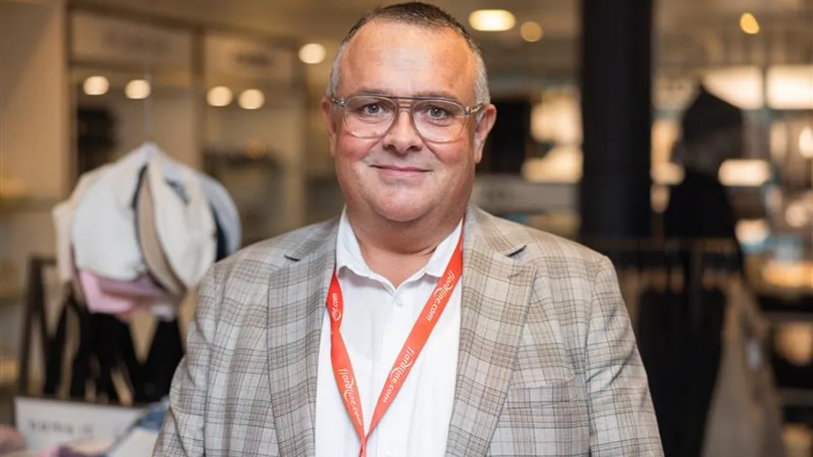 En mann med briller og nøkkelbånd står i en butikk.