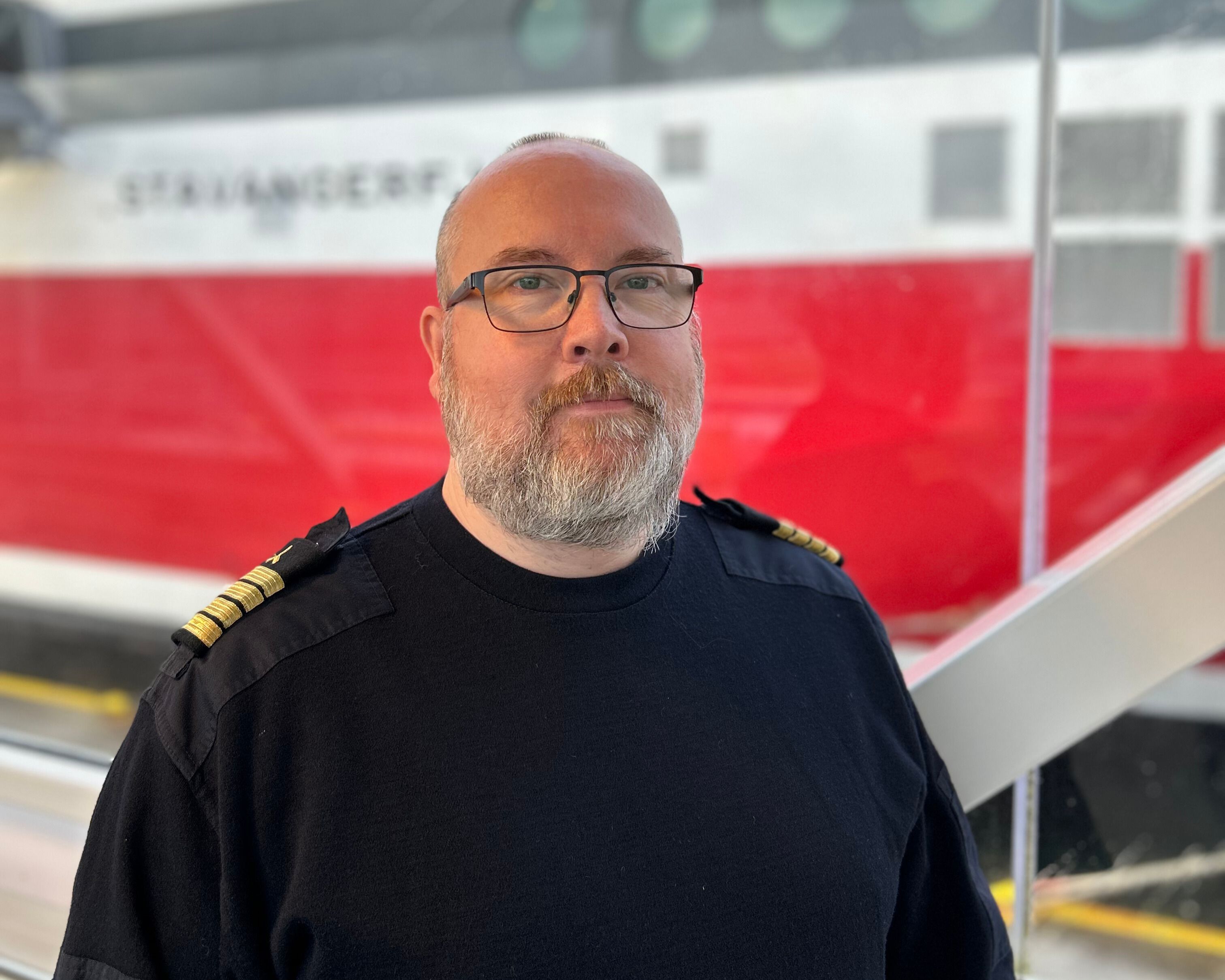 a man with a beard and glasses is standing in front of a red and white train .