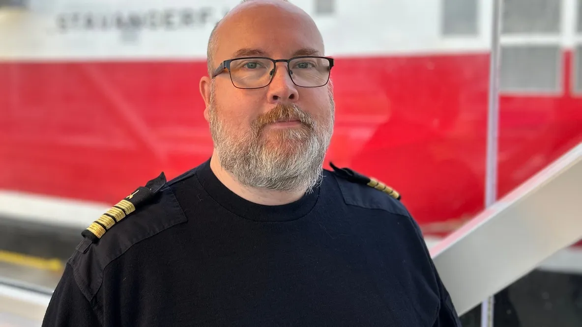 Mann med grått sjekk og briller foran et rødt skip.