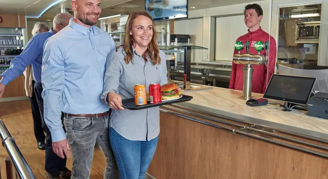 a man and a woman are standing next to each other in a restaurant holding a tray of food .