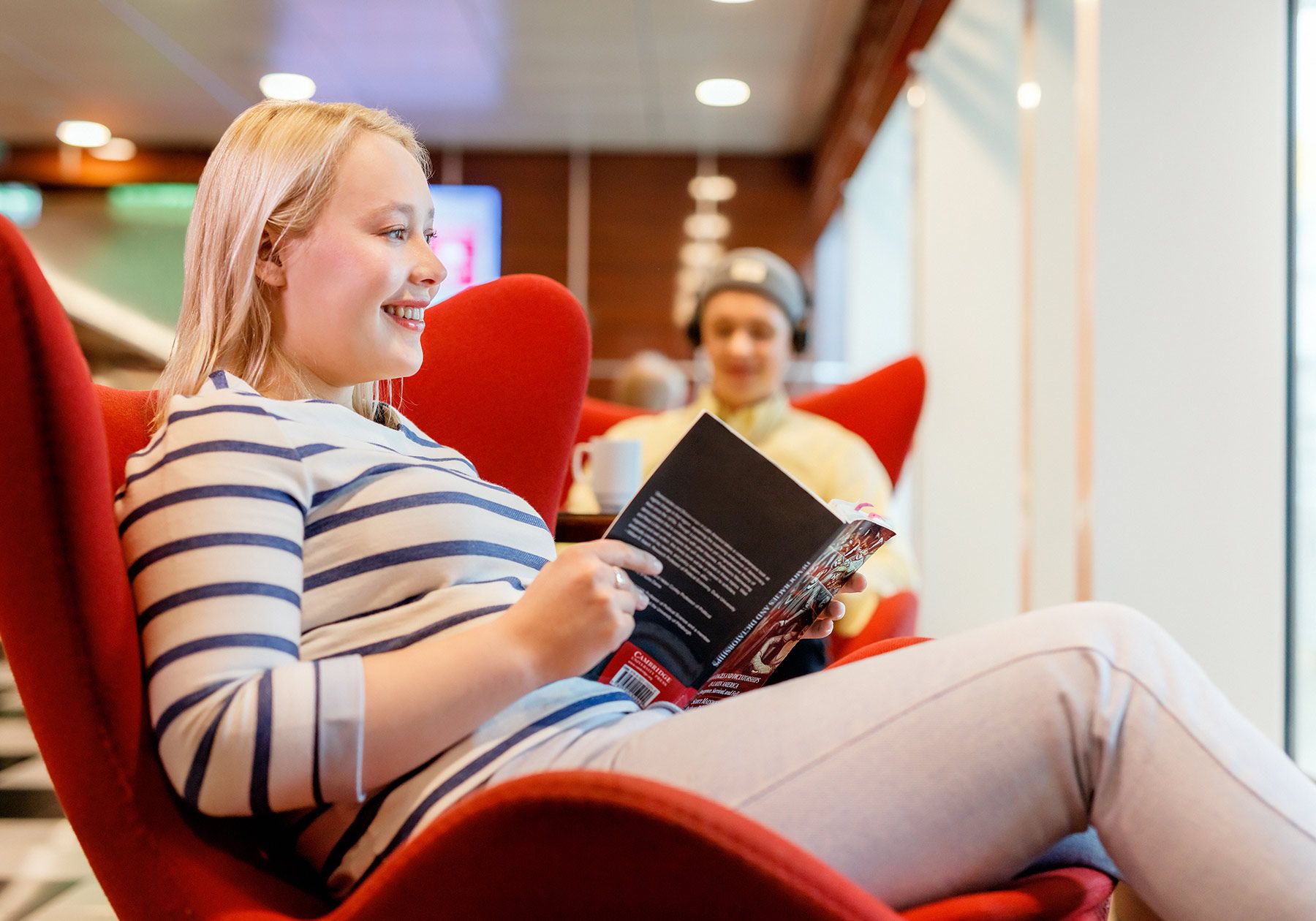 a woman is sitting in a red chair reading a book .