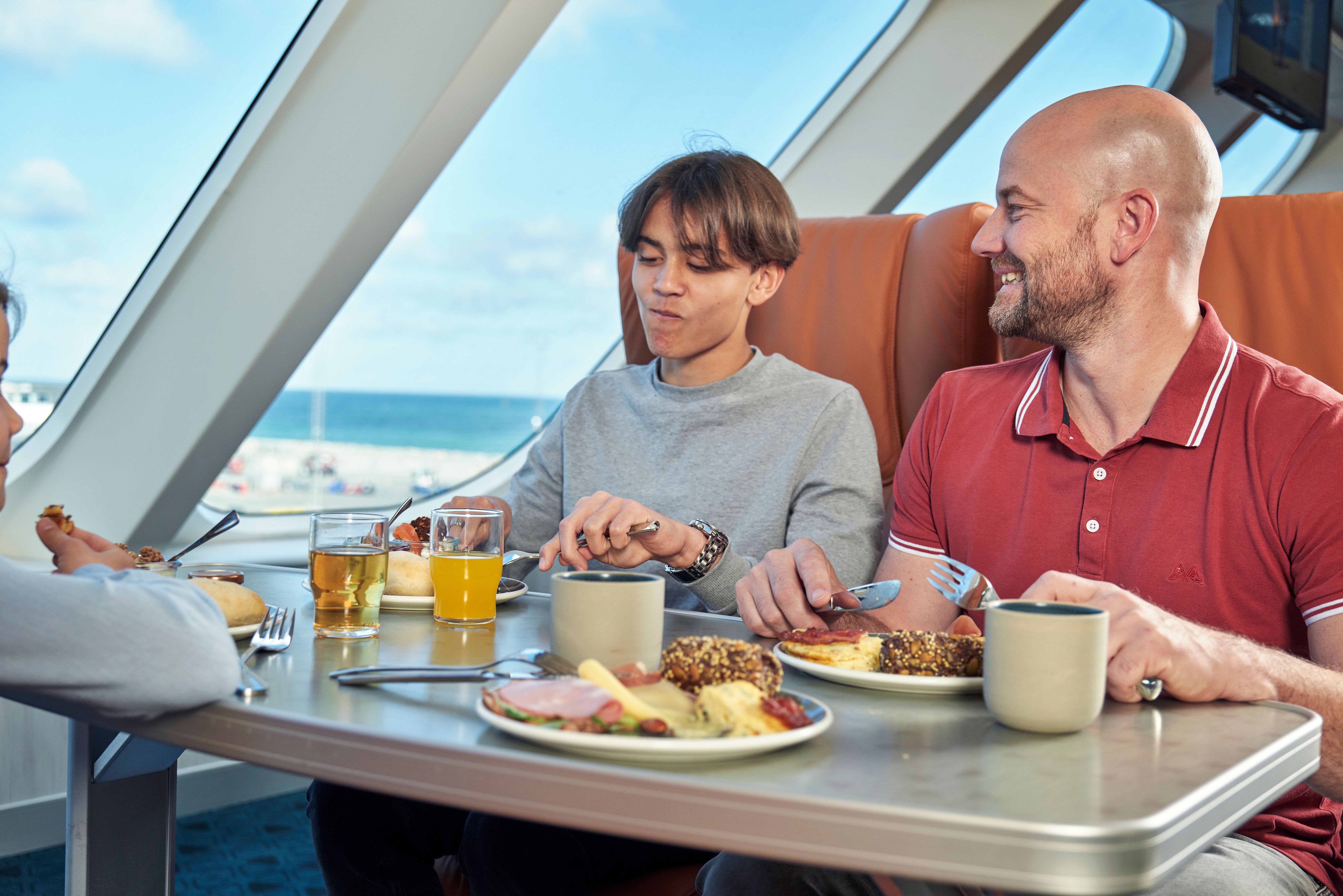 a group of people are sitting at a table eating food on a cruise ship .
