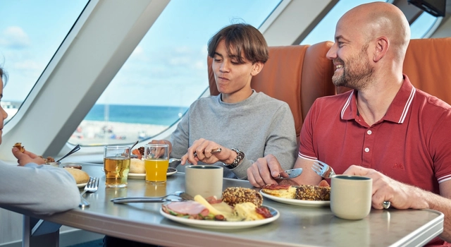 a group of people are sitting at a table eating food on a cruise ship .