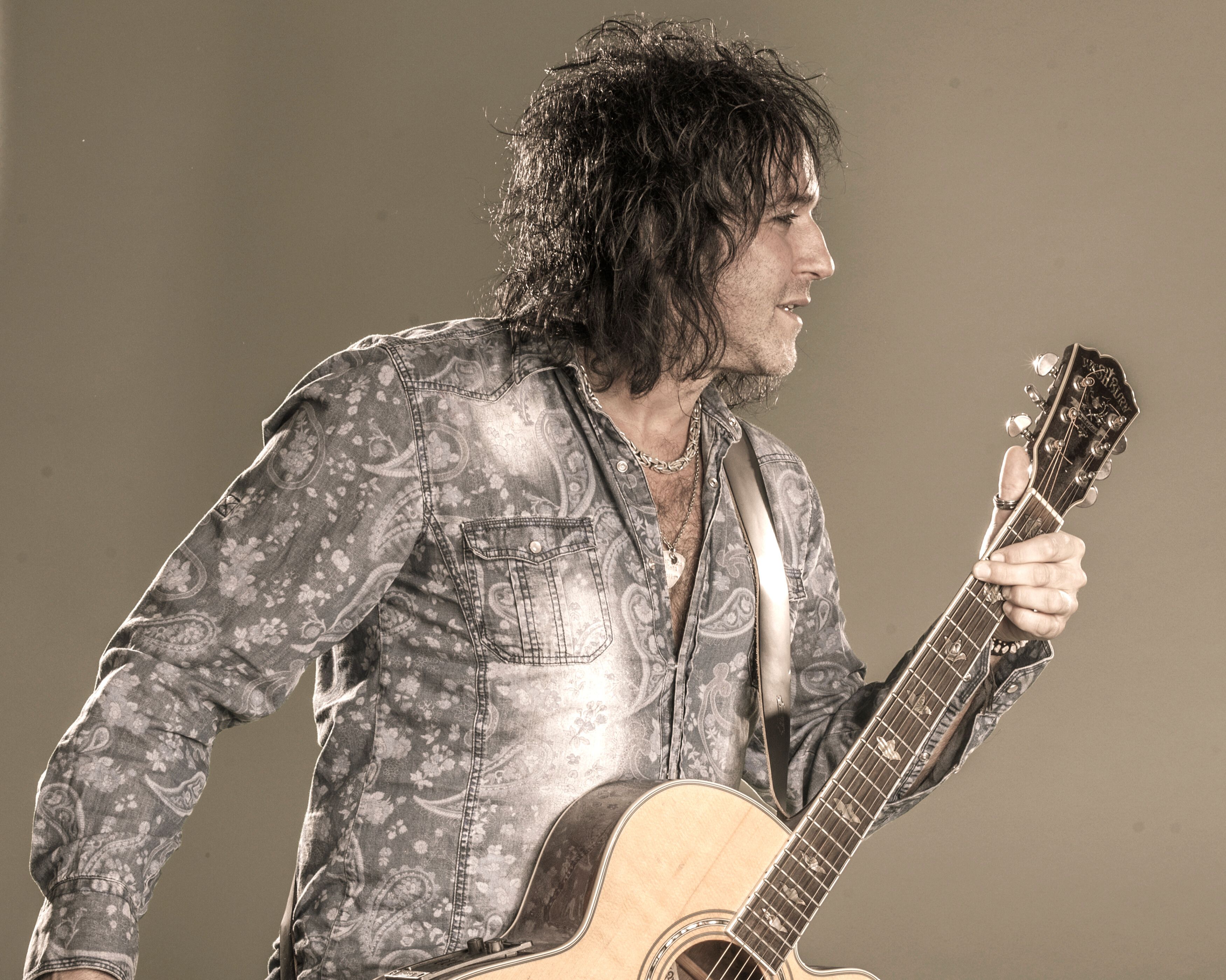 Mann med mørkt hår og gitar.