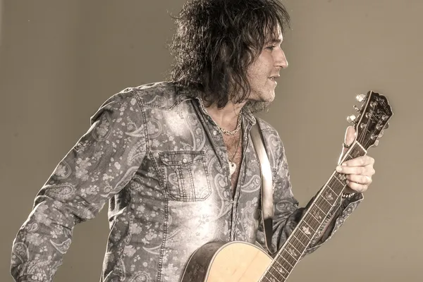 Mann med mørkt hår og gitar.