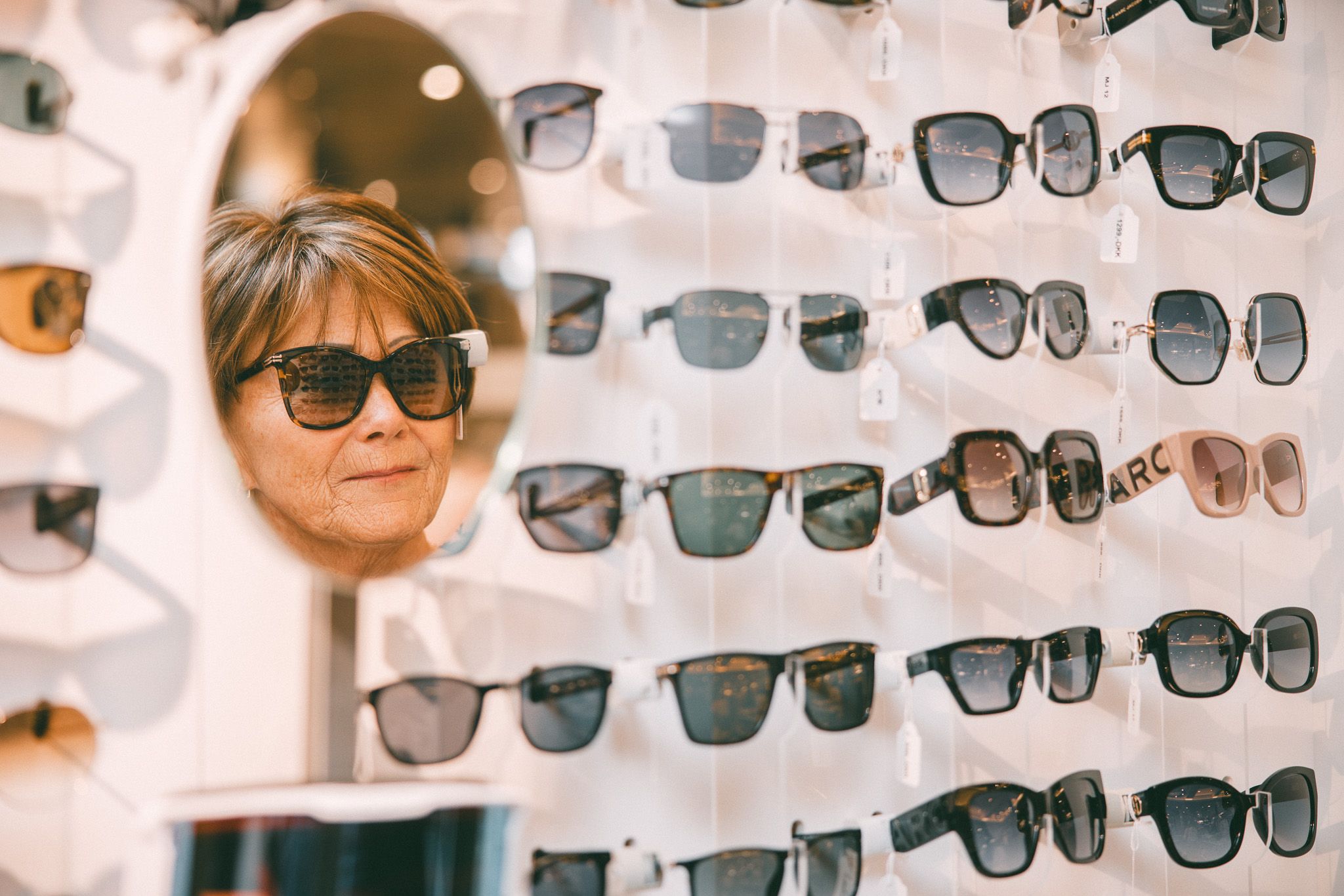 Dame prøver solbriller og ser seg i speilet.