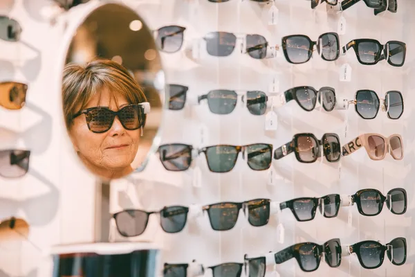 Dame prøver solbriller og ser seg i speilet.