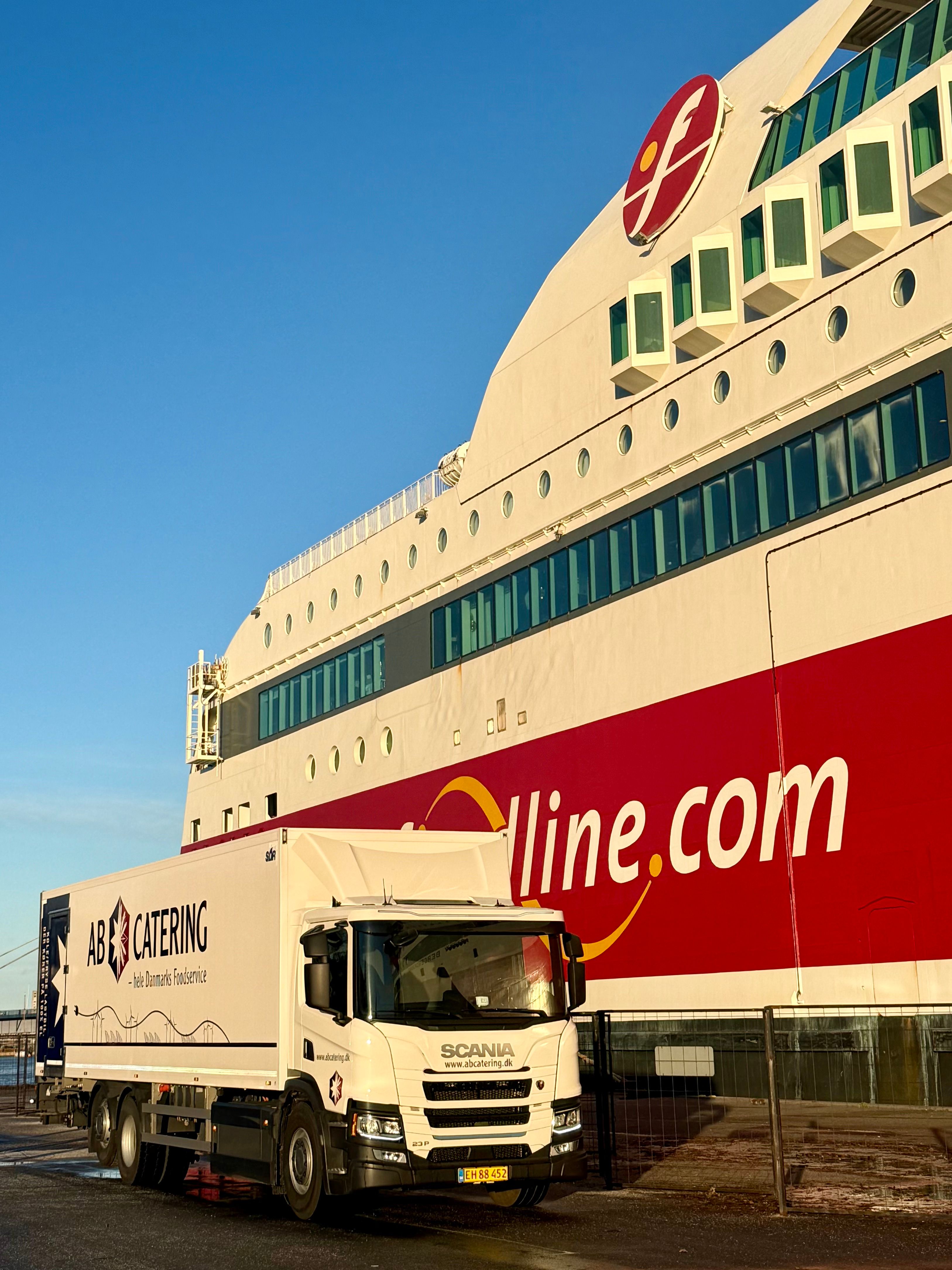 A white AB Catering truck is parked next to a large red and white Fjordline ferry.