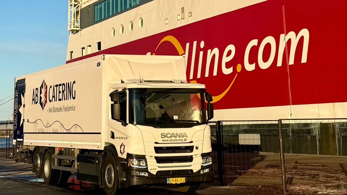 A white AB Catering truck is parked next to a large red and white Fjordline ferry.
