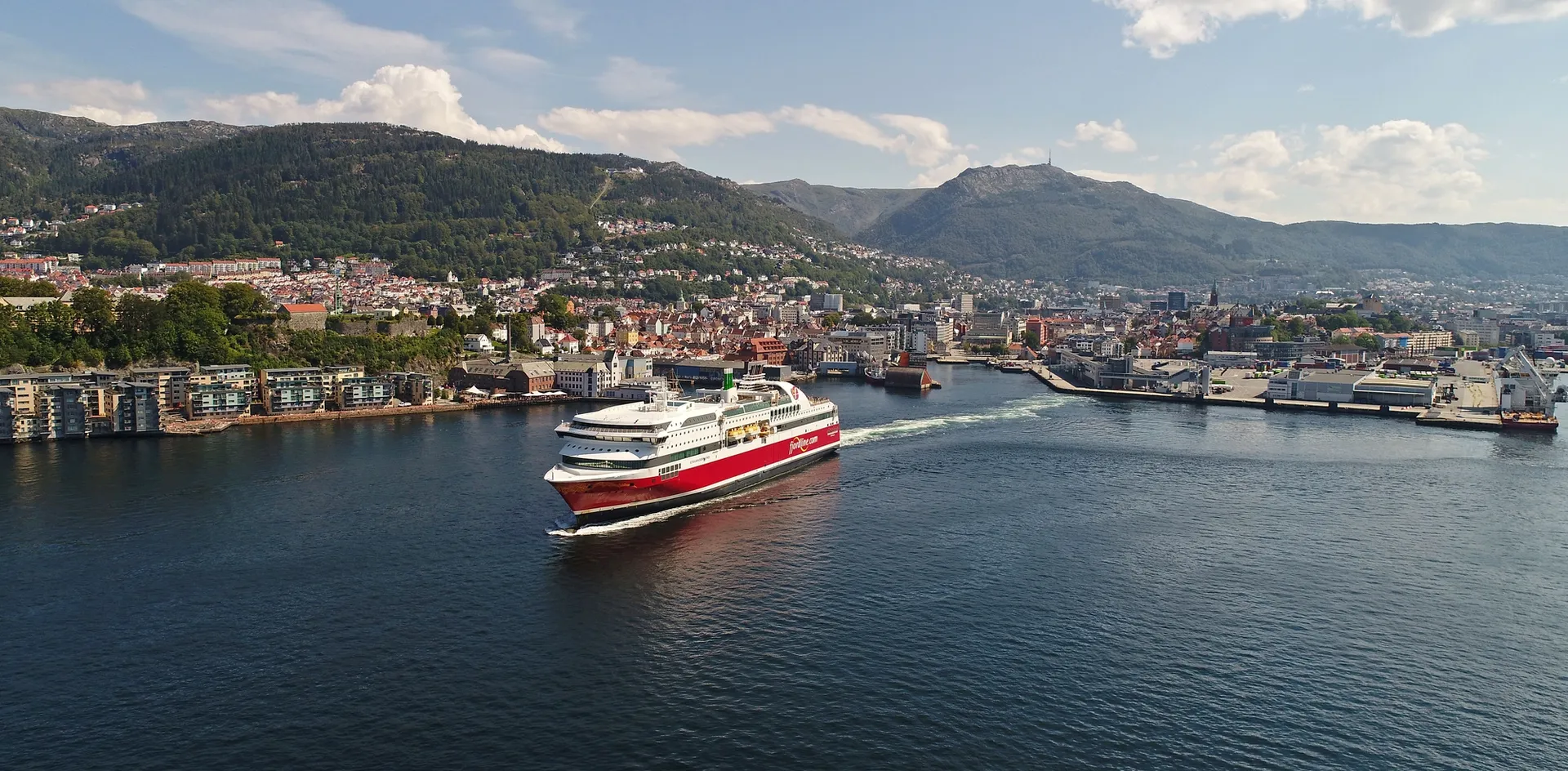 Rødt og hvitt skip på vei ut fra havnen i Bergen.