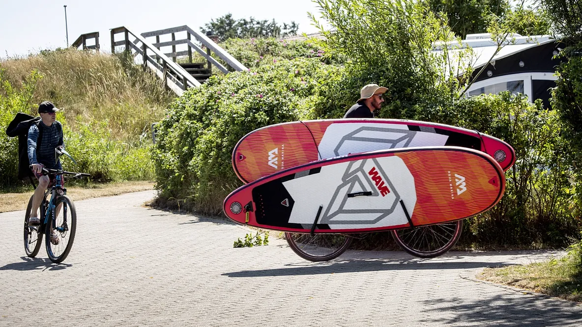 en mann sykler nedover en vei med to surfebrett