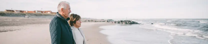 Eldre par ser utover havet på stranden.