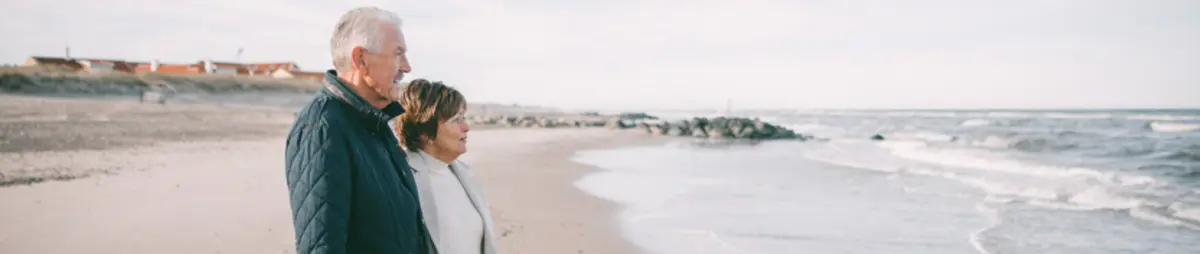Eldre par ser utover havet på stranden.