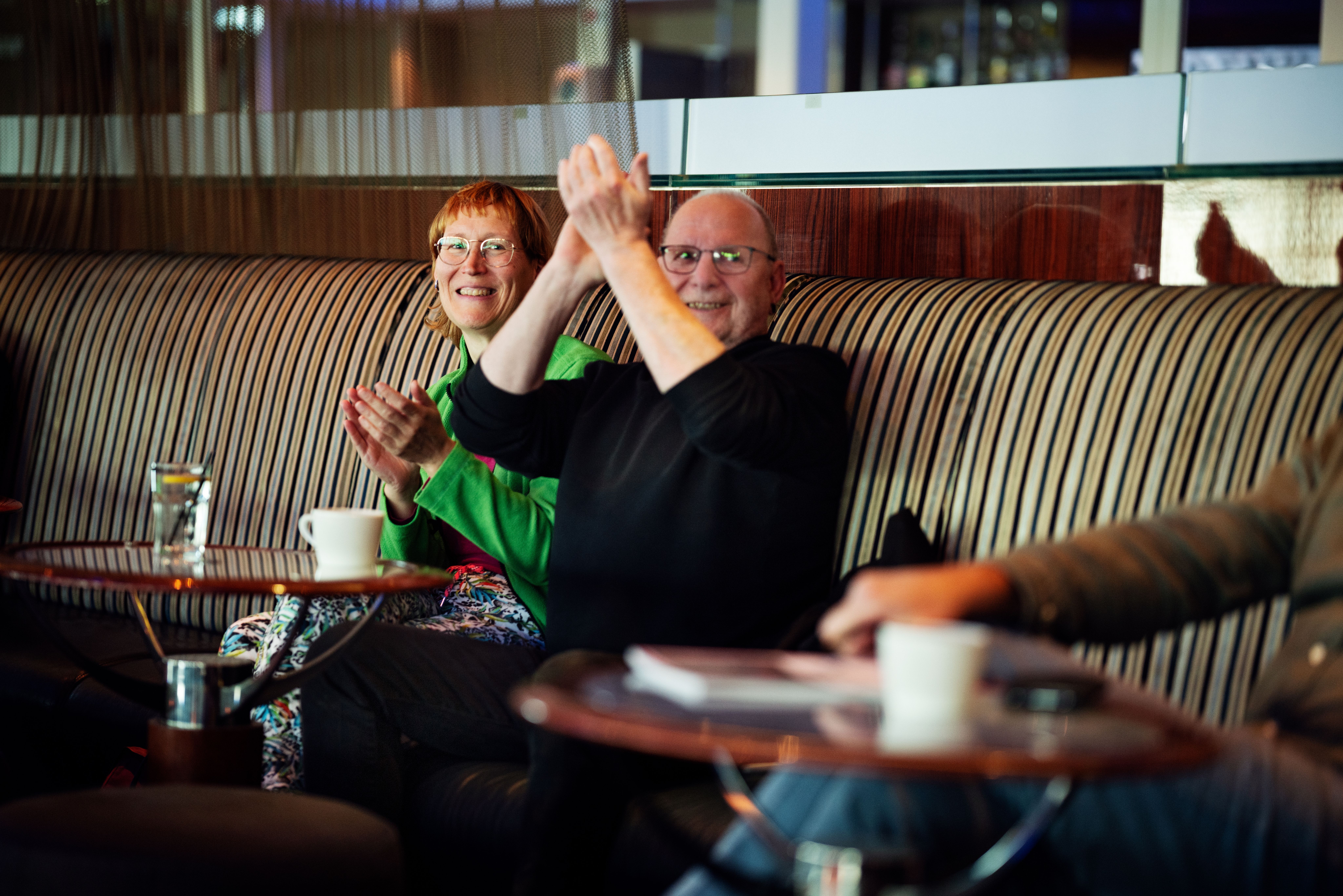 a man and a woman are sitting on a couch clapping their hands .