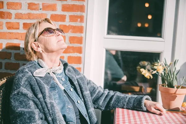 Dame sitter i sol med solbriller på.