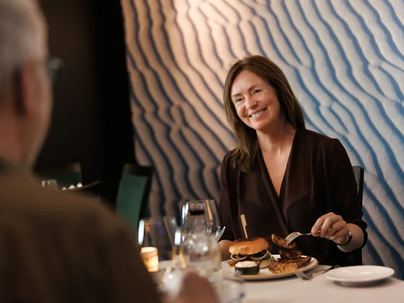 a woman is sitting at a table in a restaurant eating a hamburger .