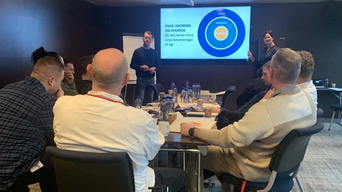 a group of men sit around a table with a man giving a presentation