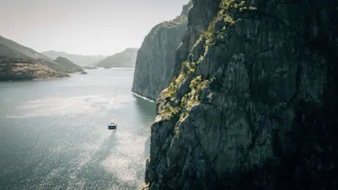 A boat on a sunny fjord between steep rocky cliffs.