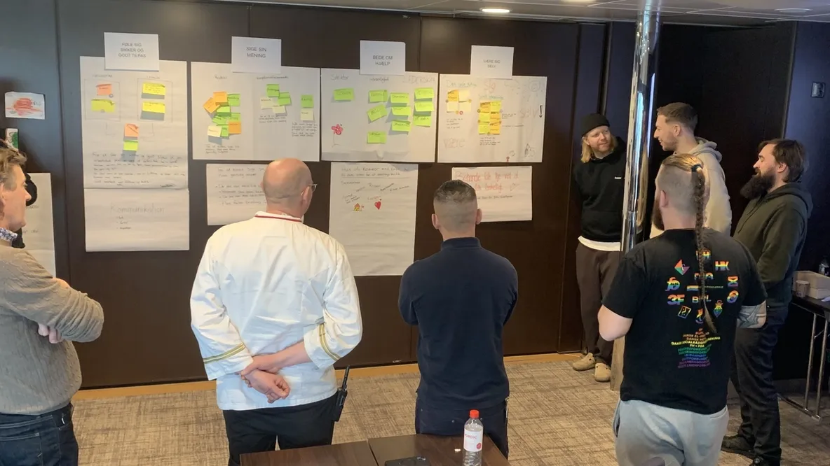a group of men are standing around a table in front of a wall with sticky notes on it .