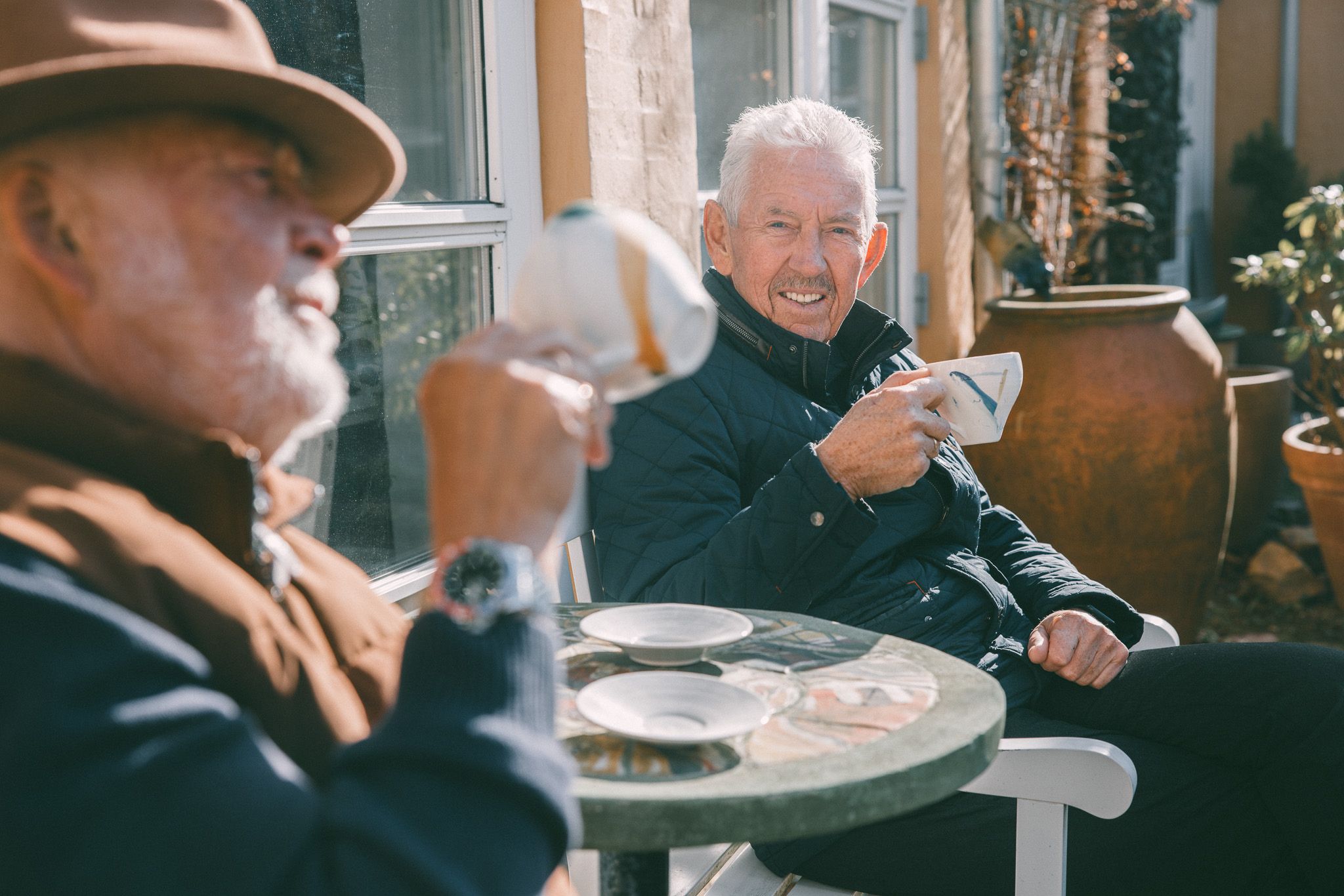 To menn sitter utendørs og drikker kaffi.