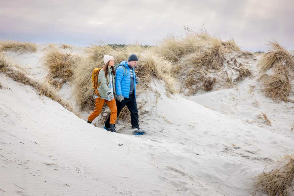 Ein Paar genießt einen ruhigen Spaziergang durch die Sanddünen an einem kühlen Tag.