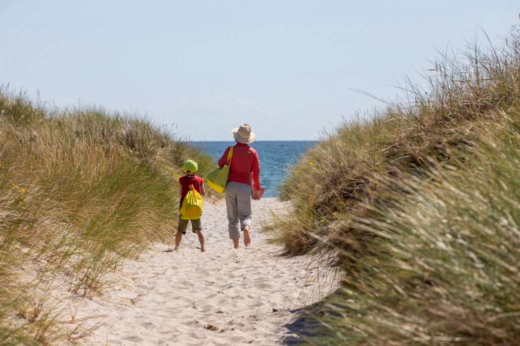 En voksen og ett barn går på sanden på vei ned mot havet.