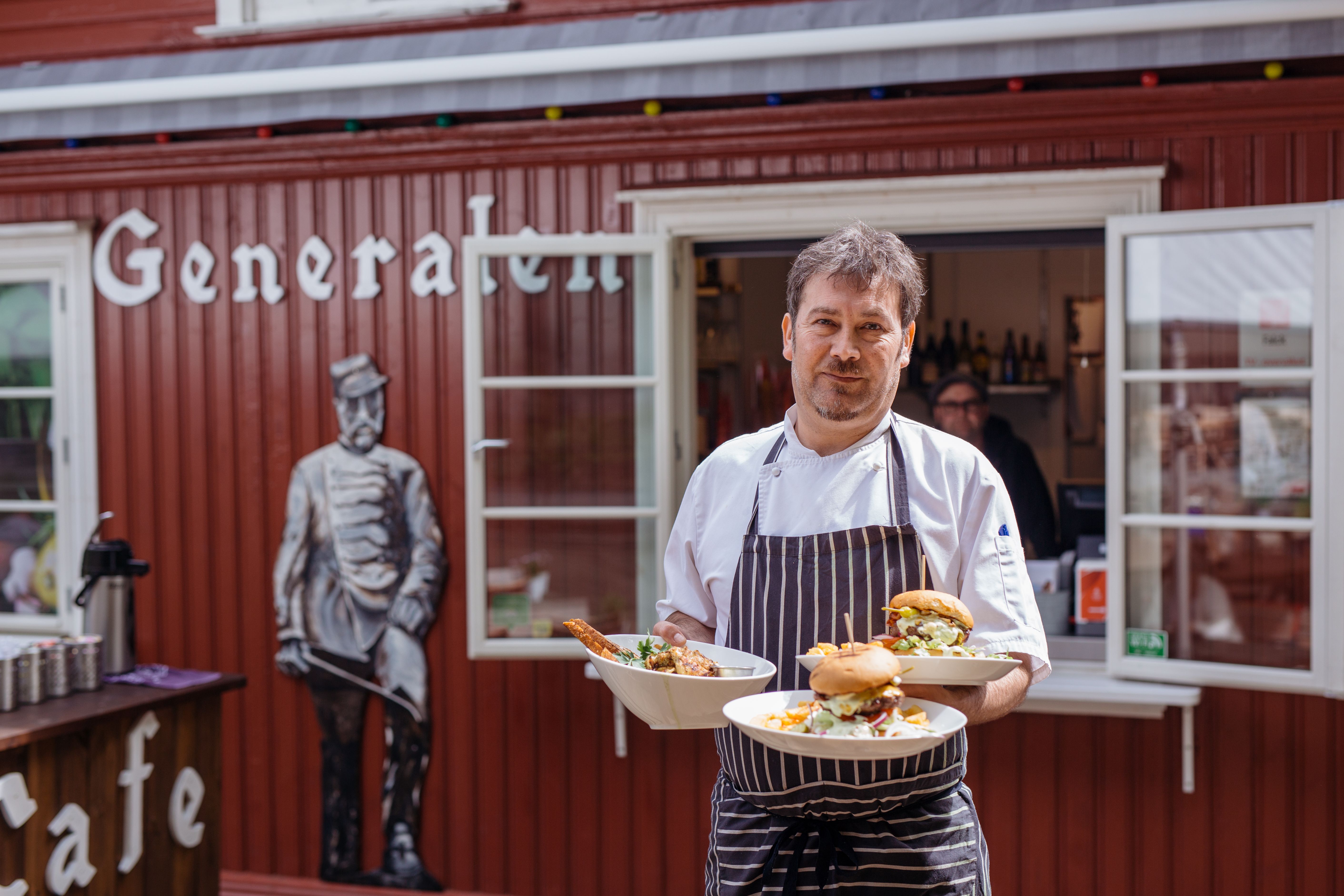 Waiter standing in front of a red building with food on plates