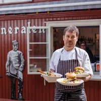 Waiter standing in front of a red building with food on plates