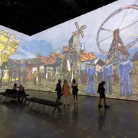 Besucher gehen in einem Kunstmuseum mit großen, farbenfrohen Projektionen von Gemälden an den Wänden herum.
