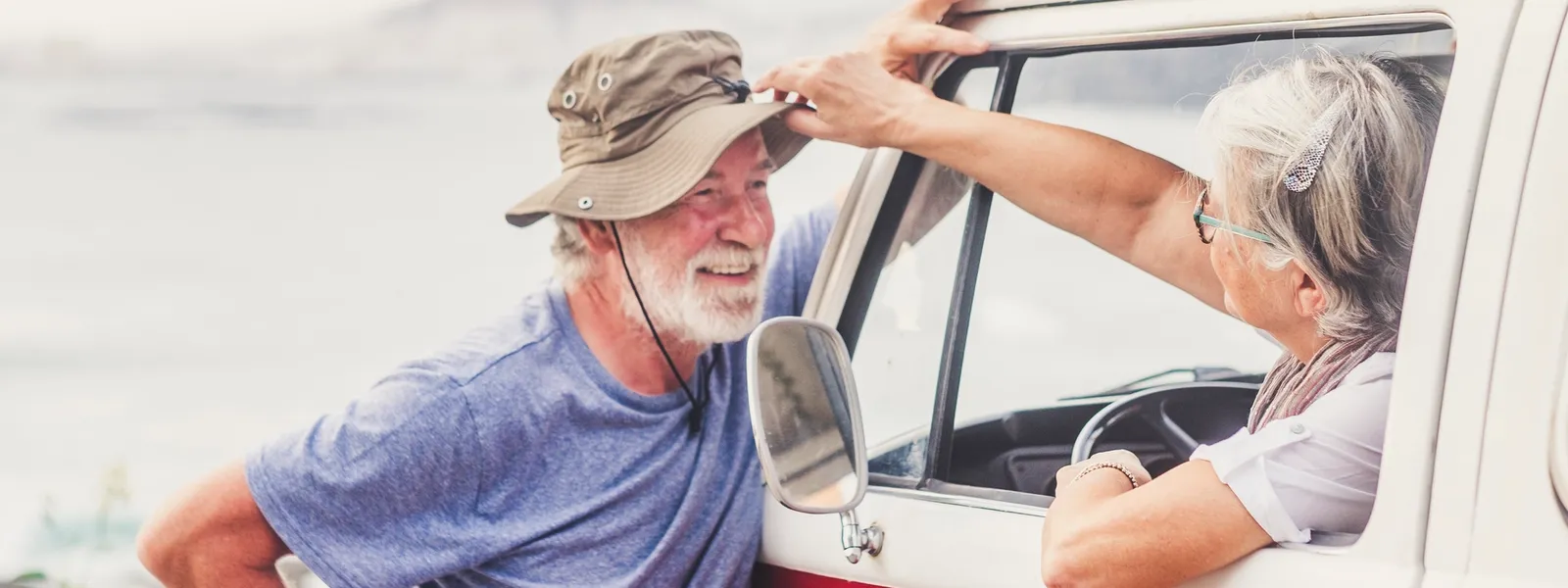 An elderly woman sits in a car and talks to a man outside the car.
